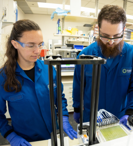 A man and woman in blue lab coats working in a lab.