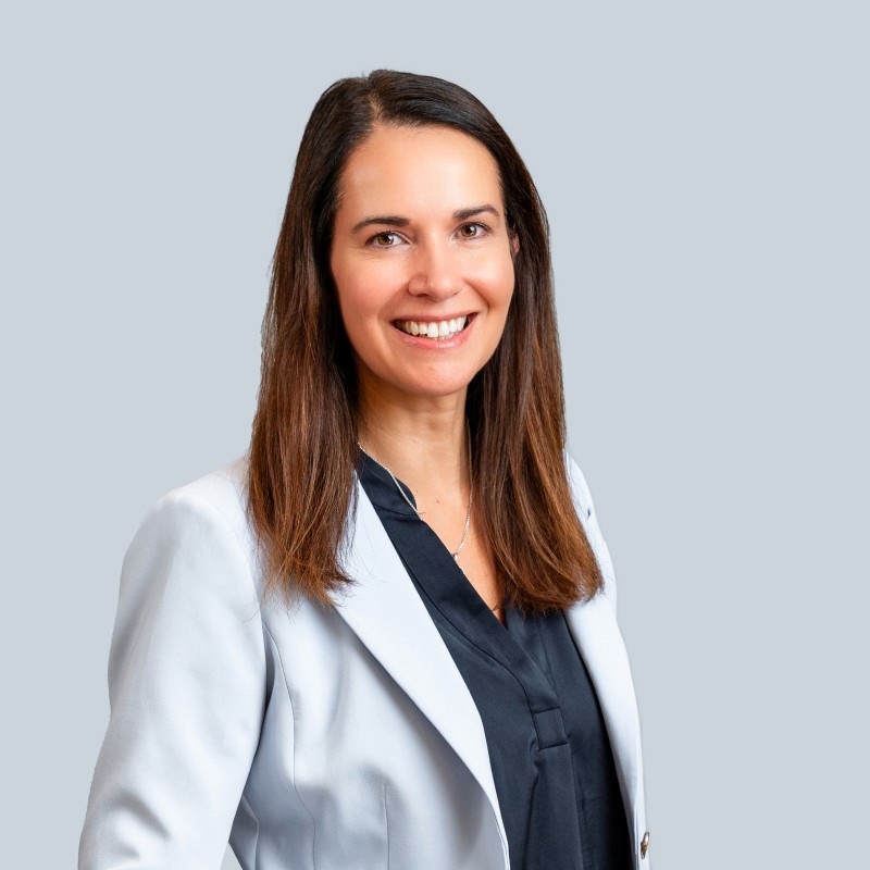 A woman with brown hair, facing the right, in a white suit jacket with a dark shirt underneath.